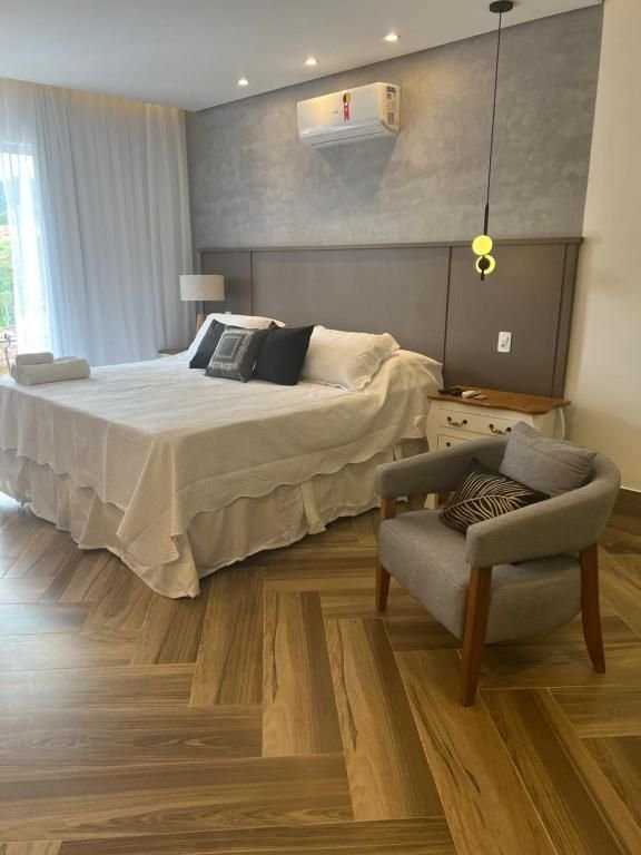 Suíte Deluxe com cama de casal, poltrona e piso de madeira em espinha de peixe